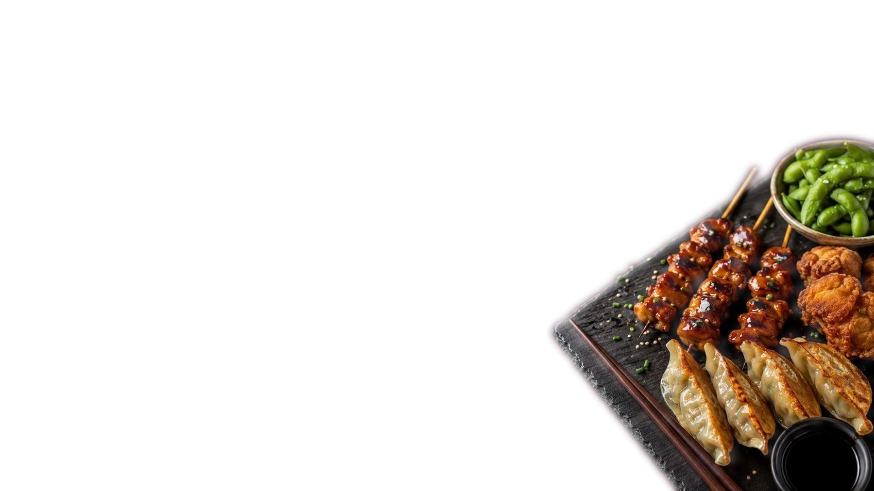 Gebratene Gyoza, glasierte Yakitori-Spieße, Karaage und eine Schale Edamame auf einer Schieferplatte vor hellem Hintergrund